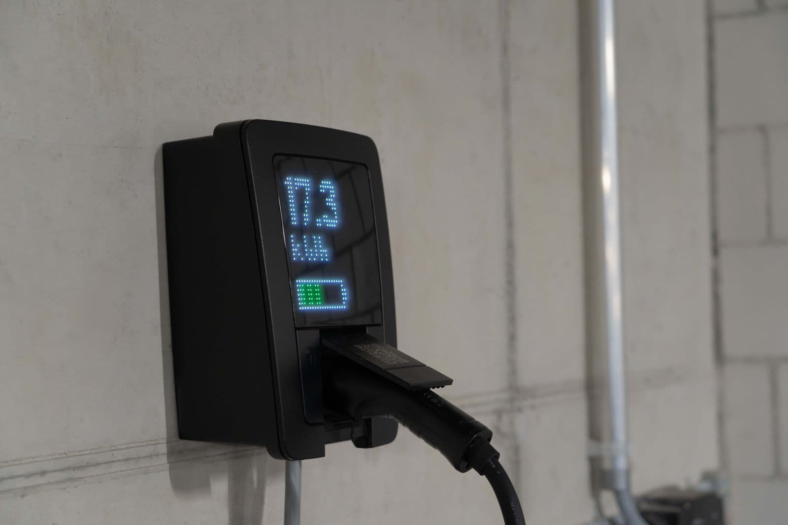A wall-mounted Level 2 EV charger with a lit display showing live charging power, plugged into a car