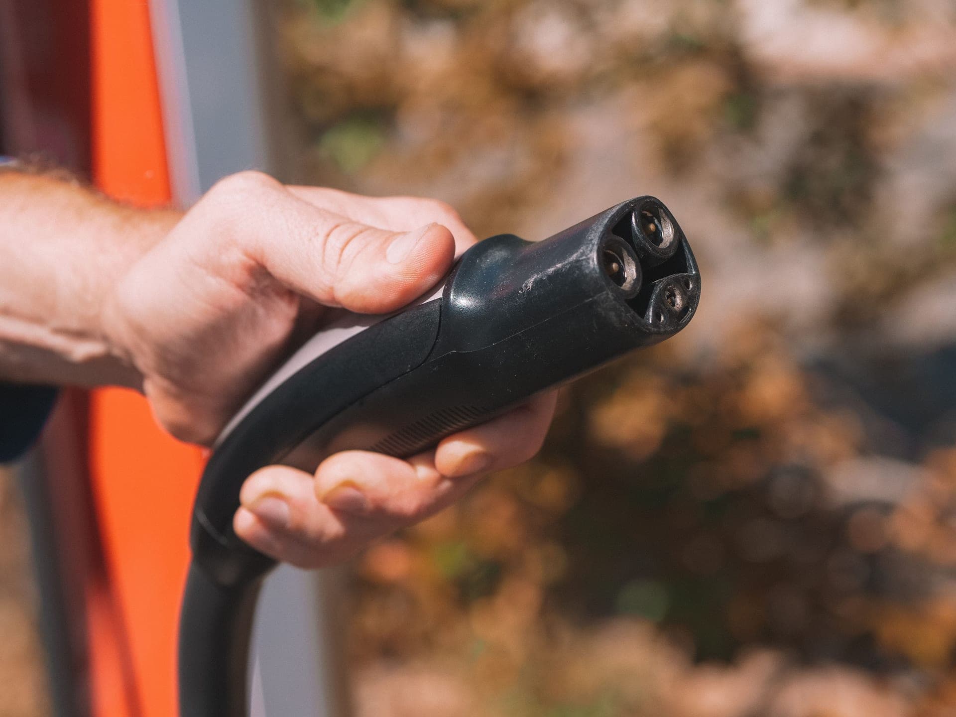 A close-up of an EV charging connector being held near a charge port